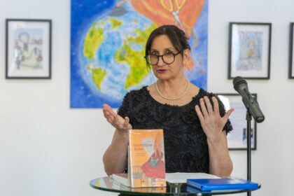 Die Künstlerin Caro Scharrer vor ihren Bildern. Auf dem Tisch vor ihr liegt das Buch 