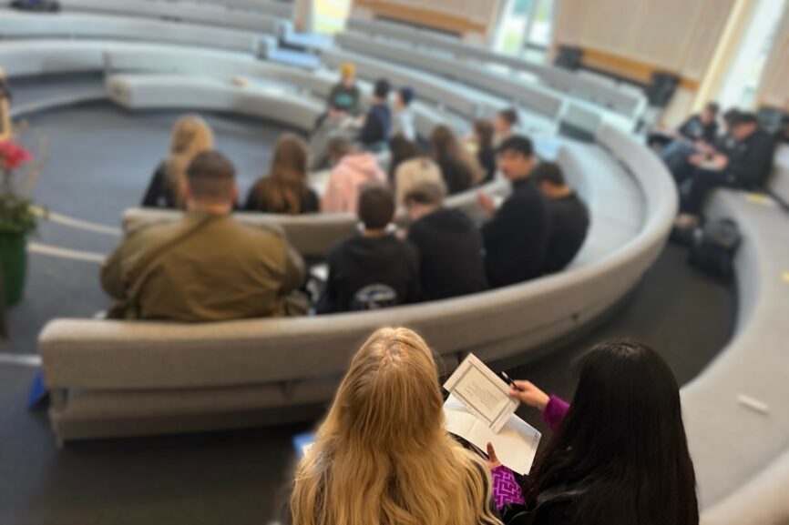 Jugendliche bei einer Gruppenarbeit in der Rotunde der Evangelischen Akademie Tutzing. Von hinten fotografiert. Man erkennt im Vordergrund zwei junge Frauen, die etwas schreiben. Im Hintergrund sind weitere Jugendliche, die unscharf sind.